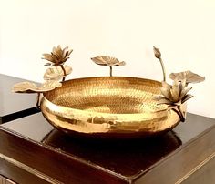 a golden bowl sitting on top of a wooden table next to a planter with leaves