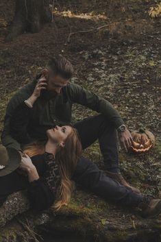 a man and woman sitting on the ground in the woods talking on their cell phones