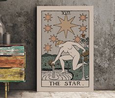 the star tarot card is on display next to a table with a vase and lamp