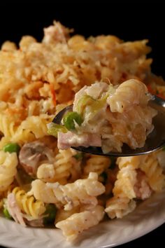 a spoon full of pasta and vegetables on a white plate with a black back ground