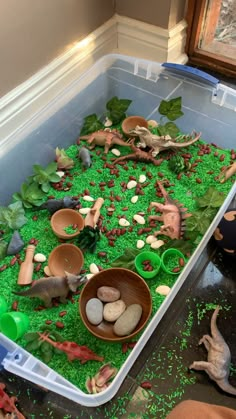 a plastic container filled with lots of green grass covered in small rocks and plants next to a window