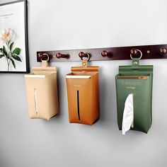 three different colored paper bags hanging on a wall with a coat rack in the background