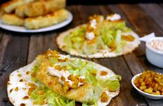 three tacos with lettuce, beans and sauces on them sitting on a wooden table