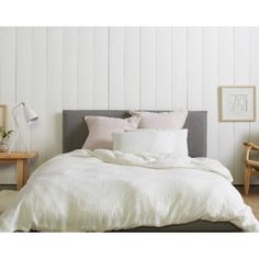 a bed with white linens and pillows in a small room next to a chair