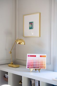 a desk with a lamp, paint swatches and a painting on the wall behind it