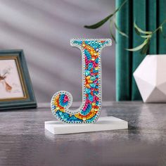 the letter j is decorated with multicolored beads and sits on a wooden table