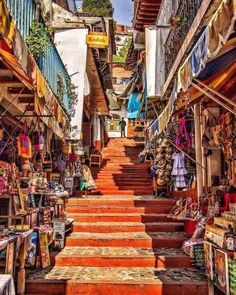 an alleyway with stairs and shops in the city, surrounded by colorful fabrics on display