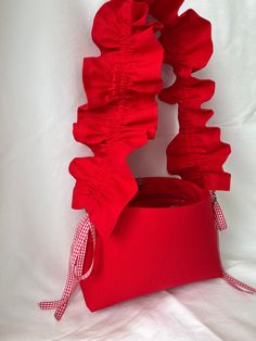 a red bag with ruffles on it sitting on a white sheeted surface