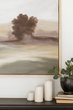 a painting hanging on the wall above a mantle with candles and a potted plant