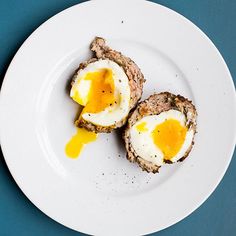 two pieces of meat with an egg in the middle on a white plate against a blue background