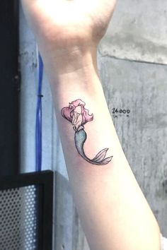 a small mermaid tattoo on the wrist with a flower in it's left hand