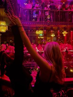 a woman reaching up into the air in front of a room full of people and chandeliers