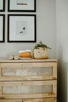 a wooden dresser topped with a potted plant next to two framed pictures on the wall