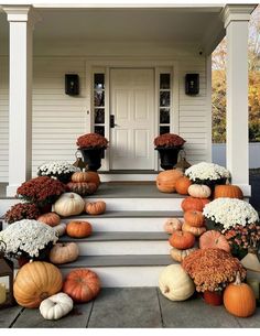 a front porch with pumpkins and mumins on the steps, in front of a white house