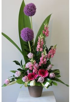 an arrangement of flowers in a vase on a table with green leaves and pink carnations