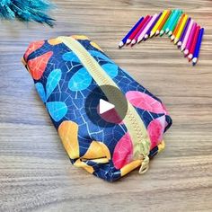 a pencil case sitting on top of a wooden table next to some colored pencils