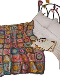 a crocheted blanket on a bed next to an open book and eyeglasses