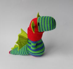 a stuffed toy dragon sitting on top of a white table next to a green and blue striped sock