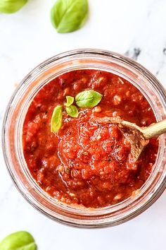 a jar filled with tomato sauce and basil leaves