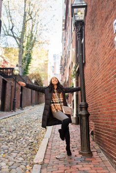 a woman leaning against a lamp post on the side of a building with her arms outstretched