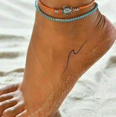 a woman's foot with two bracelets on it, and the ankle is covered in sand