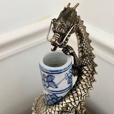 a dragon figurine sitting on top of a cup next to a window sill