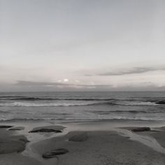 an empty beach with waves coming in to the shore and some rocks sticking out of the sand