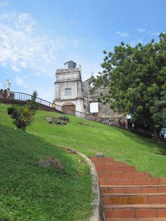 an old building on top of a hill with stairs leading up to it and trees in the foreground