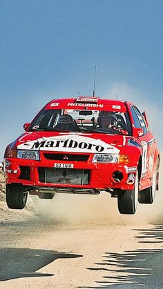 a red car is jumping in the air over sand and dirt on a sunny day