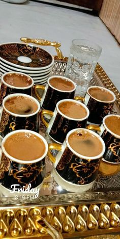 there are many cups of hot chocolate on the tray with gold trimmings and plates