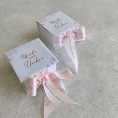 two boxes with pink ribbons tied around them on the floor, one has a name tag and the other has a bow