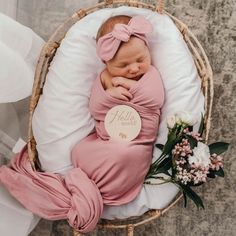 a newborn baby wrapped in a pink blanket is laying on a wicker basket next to flowers