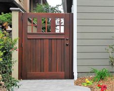 a wooden gate in front of a house with flowers and plants around the entrance area