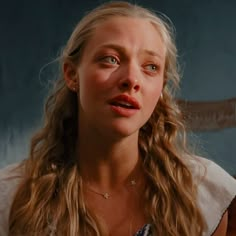 a woman with long blonde hair and blue eyes looks at the camera while wearing a necklace