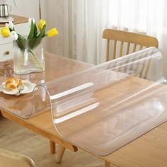 a clear glass table with yellow tulips in a vase on the dining room table