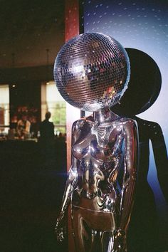 a shiny silver statue with a disco ball on it's head