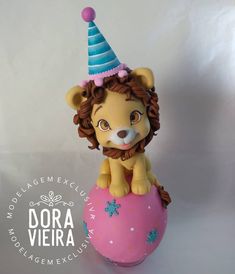 a lion figurine sitting on top of a pink ball with a blue hat