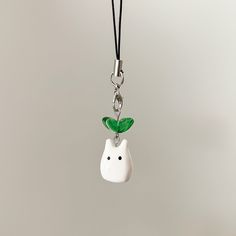 a white cat with a green leaf on it's head hanging from a black cord