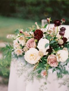 a bouquet of flowers is sitting on top of a table with white linens and greenery