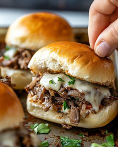 someone is picking up the meat on top of two sliders with cheese and parsley