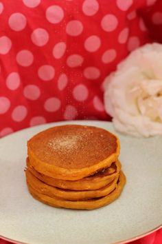 a stack of pancakes sitting on top of a white plate next to a pink flower