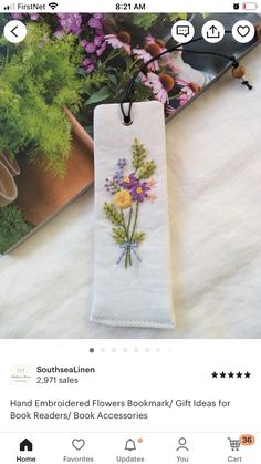 an embroidered bookmark with flowers on it sitting next to a magazine and some plants