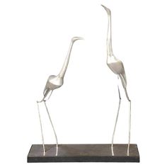 two metal birds standing on top of a black base with their necks touching each other