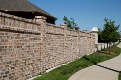 a long brick wall next to a sidewalk