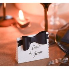 a place card with a black bow on it sitting on a table next to wine glasses