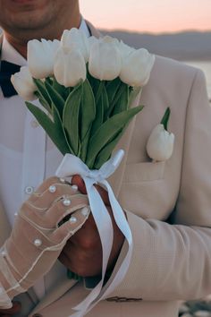 a man in a tuxedo is holding a bouquet of white tulips