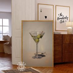 a martini glass with olives in it sitting on the floor next to framed pictures