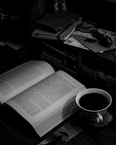 an open book sitting on top of a table next to a cup of coffee