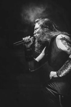 a man with long hair and tattoos on his arm holding a microphone in front of him