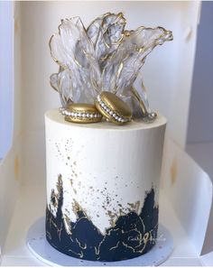 two wedding rings on top of a white and blue cake with gold leaf decorations in the middle